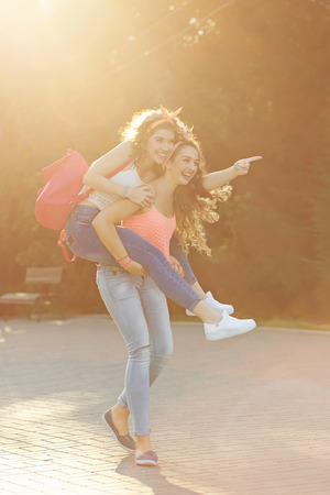 Best girlfriends for a walk. Girls carry piggyback. Girls dressed in the style of Pin-up girl. Hipster. Warm toning. The concept of true friendship.の写真素材
