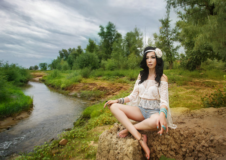 Young carefree boho girl meditates on the bank of the river. Stylish lifestyle portrait.の写真素材