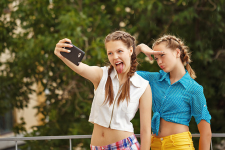 Best friends teenagers photographed in a summer park. Photo phone selfie. Girls dressed in shorts and a shirt. On summer vacation. The concept of true friendship.の写真素材