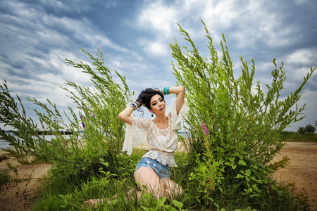 Young carefree boho girl sitting on the beach. Stylish lifestyle portrait. Photo against cloudy sky.の写真素材
