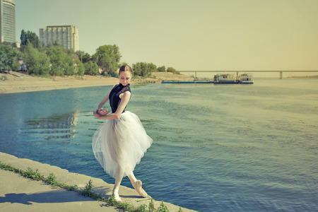 Young slender ballerina in tutu dancing on the riverbank. Summer day. The concept modern ballet. Performance on the street.の写真素材