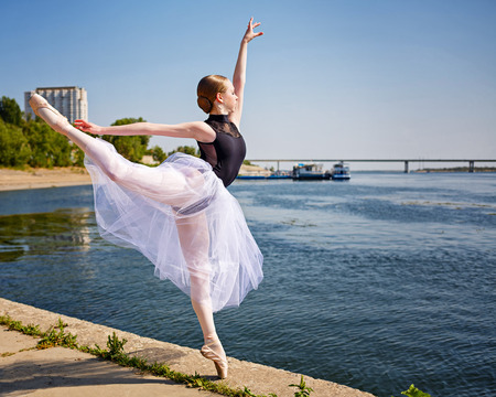 Beautiful ballerina dancing on the riverbank. Summer day. The concept modern ballet. Performance on the street.の写真素材