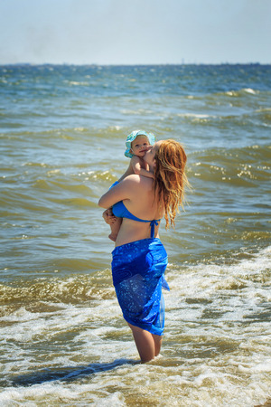 Young mother with her baby in her arms, standing on the beachの写真素材