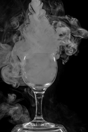 Abstract art. Hookah smoke into cocktail glass on a black background. Witch potion background for Halloween. Unusual bar drink. Drink in the glass with the effect of dry ice.の写真素材