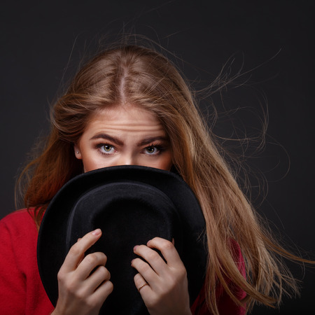 Young attractive girl hides her face behind a hat. Expressive look of beautiful eyes. Flirty. Youth fashion.の写真素材