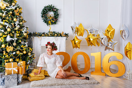 A girl sitting on the carpet next to the Christmas tree and presents.