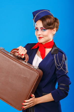 Stewardess with face art holds suitcase. Young attractive girl in a blue suit flight attendants. Airfreight. Service. Baggage.の写真素材