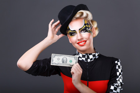 Girl taxi driver holding a dollar. Lovely girl in a hat and face art. On a gray background.の写真素材