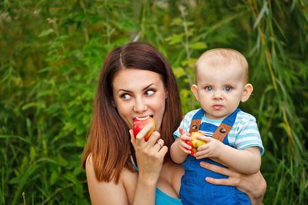 Young mother and daughter in the park. Picnic. Happy family, childhood and motherhood. Mother and child eating apples. Portrait.の写真素材