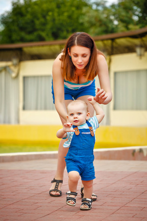 Daughter is learning to walk. Mother holding the baby's hands. Walk in the park. The happiness of motherhood. Happy childhood.の写真素材