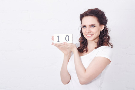 Young cute girl smiling and holding a number ten. Girl dressed in a white t-shirt. Emotional expression.の写真素材