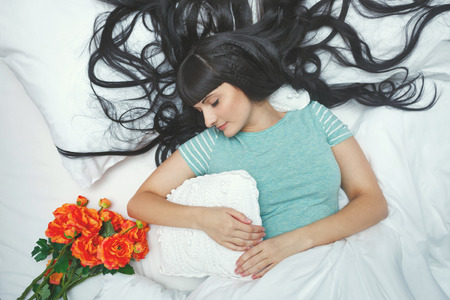 Cute girl sleeping in bed. Bedroom. Hair spread on the pillow. Undisturbed sleep. Recreation. Flowers on the bed.の写真素材