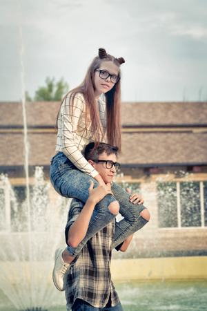 Sweethearts teenagers. Girlfriend and boyfriend together. They wear glasses. Warm toning. The boy put the girl on his shoulders. Piggyback. First love. He falls in love. Date.の写真素材