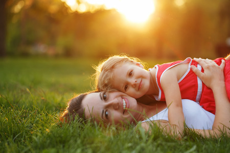 Mother and daughter lying on the lawn. Family in the city park outdoors. Happiness of motherhood and childhood.の写真素材