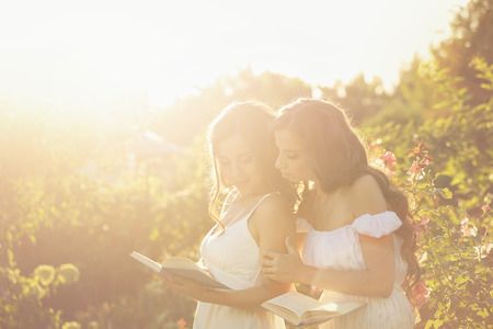 Two sisters read books in the backyard. Girl showing her sister something interesting in his book. Shoot in the rays of the setting sun. Soft focus and creative effects.の写真素材