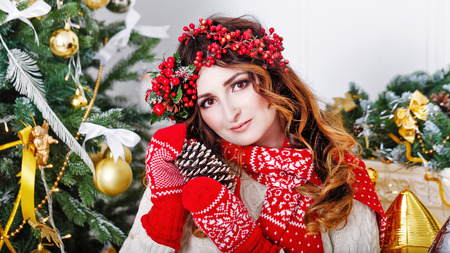 Pretty girl in a scarf and gloves holding a pine cone at the Christmas tree. The festive mood.の写真素材
