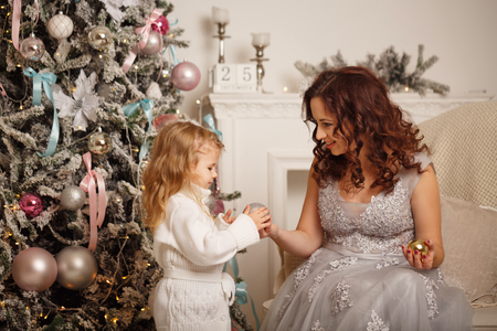 Mother and daughter near a Christmas tree. Mother helps daughters decorate Christmas tree. Family celebration. Happy Motherhood and Childhood.の写真素材