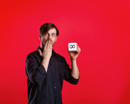 Man holding cube with the sign of infinity. Numerals. A man shows a cube with the sign of infinity. He was surprised and covers her mouth.の写真素材