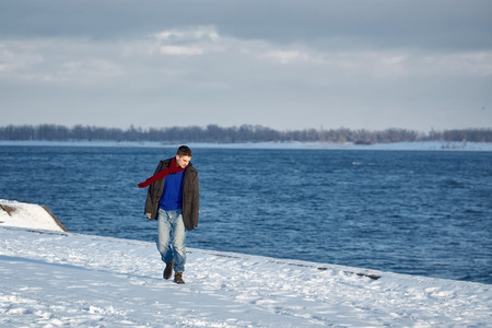Man goes along the promenade. He is dressed in coat, scarf, jeans and gloves. Winter.の写真素材