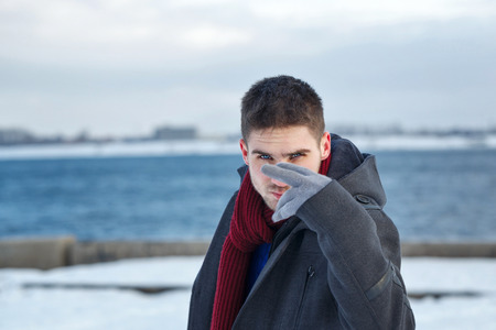 Man looks into the camera. He is dressed in coat, scarf and gloves. Winter.