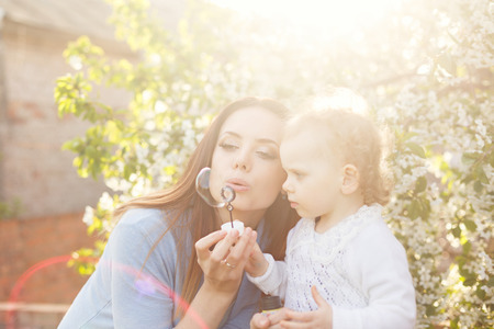 Mother and daughter inflate soap bubbles. Family portrait in backlight. Spring mood. Family timeの写真素材