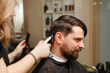 Professional hairdresser doing haircut men's hair. Cutting electric razor. Beauty saloon. Male beauty. The client is a hipster.の写真素材