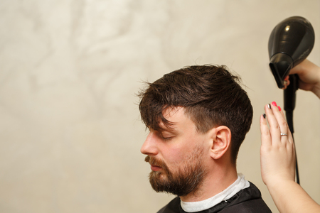Professional hairdresser doing haircut men's hair. Drying hair with a hairdryer. Beauty saloon. Male beauty. The client is a hipster.の写真素材