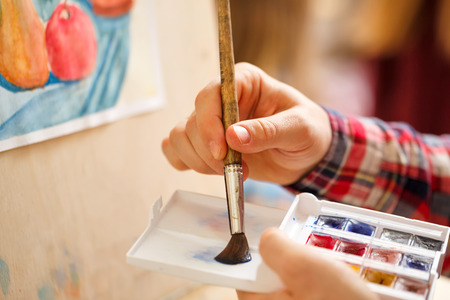 Artist mixes watercolors on a plastic palette. Hand and brush close-up. Brush of a hair pony.の写真素材