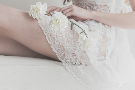A nice girl is holding white flowers on her knees. She is wearing a white dress. The bride is waiting for the ceremony. Man is unrecognizable.の写真素材