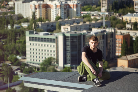 The roofer rests after climbing to the roof. Active way of life in urban space. Courage and adrenaline.の写真素材