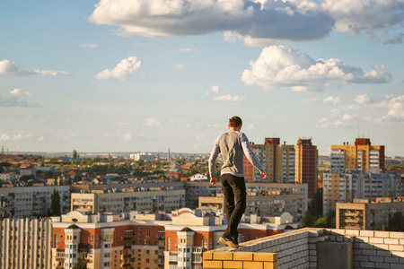 A lone roofer walks along the edge of the roof fence on a high-rise building. Courage and adrenaline.の写真素材