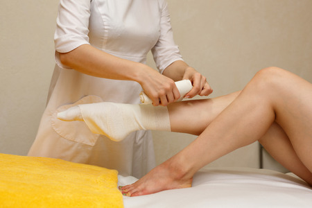 Spa treatment. STYX wrap. Anti-cellulite treatment. The cosmetologist wraps the feet of the client.の写真素材