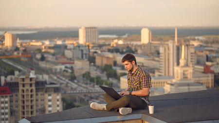 Man with a laptop is drinking coffee on the roof. Freelancer at work.の写真素材