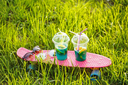 Two fruit cocktails stand on the skateboard. Sunglasses lie on the skateboard. Skate stands in the green grass. A refreshing drink.の写真素材