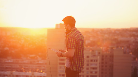 Hipster man listening to music with headphones on the roof at sunset. Philosophical Reflectionsの写真素材