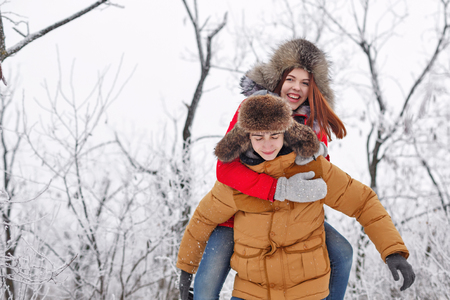 Couple in love. Teenagers on a date outdoors in the winter. He rolls his girlfriend Piggyback. She...