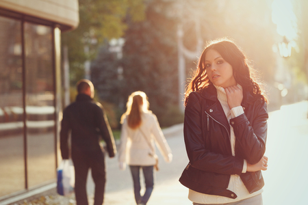 A teenage girl in a leather jacket and sweater stands on the mall. The back light of the setting sun highlights her hair. Young and stylish.の写真素材