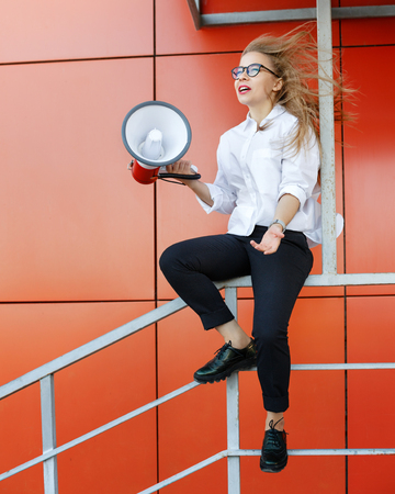 A young attractive girl in a white shirt and glasses is holding a loudspeaker in her hands. Protest actionの写真素材