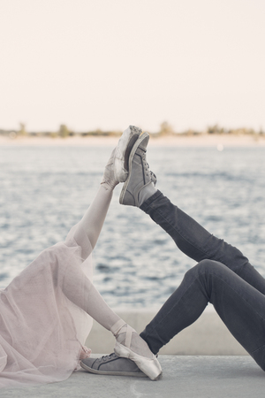 A couple in love on a date. The guy is an athlete in sneakers and a ballerina in pointe shoes. They lie on the ground. Leg to foot. Sports and dancing.の写真素材