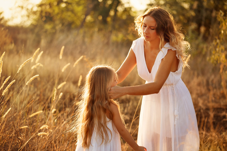 Family, mother and daughter are walking in the meadow. Mother corrects her daughter's hair. They are blondes. Family time together.の写真素材