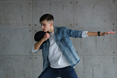 Teenage guy wearing denim jacket and white sweater is dancing hip-hop with baseball cap. Dynamics of modern dance movement. Youth fashion.の写真素材