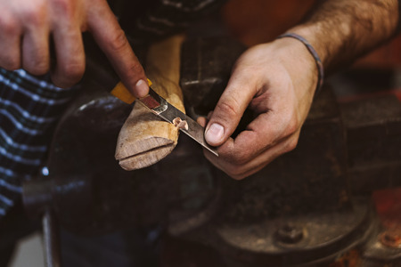 Man works in carpentry workshop. He cuts off excess with knife tree with wooden handle of an ax. Men...