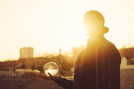 Contact juggling. Man balancing glass bowl on hand. Inverted panorama of city and sky in reflection of ball. Mastery of representation. Photo at sunset.の写真素材