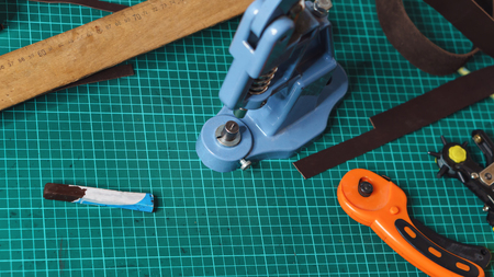 Working tools of tanner. Punch, riveter, knife and ruler lie on carpet for cutting. Workflow in...