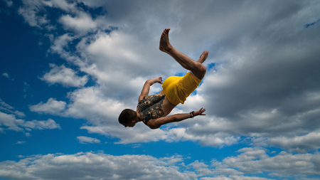 Tricking on street. Martial arts. Man performs jump with flip-flop barefoot. Shooted from bottom foreshortening against sky.の写真素材