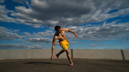 Tricking on street. Martial arts. Man performs leap with support of his hand barefoot. Shooted from bottom foreshortening against sky.の写真素材