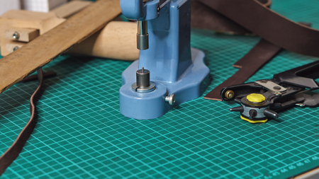 Tools tanner on desktop in workshop. Close-up. Punch, riveter, ruler and pieces of leather lie on...