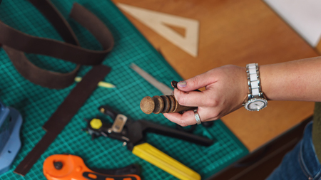 Tanner holds slicker and leather blank in her hands. In background lie knife, punch and rulers....