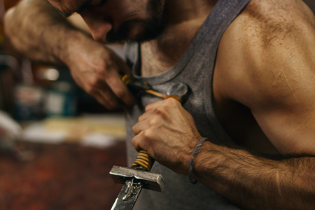 Blacksmith fastens leather winding of sword. Man is working in workshop. He fixes the leather band...