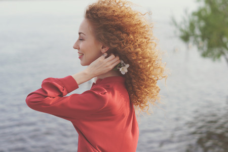 Girl with curly hair. She fervently laughs and holds white flower in her hands. Spring time. Close-up portraitの写真素材